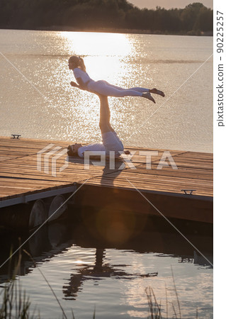 Beautiful young couple doing acro yoga on the pier against sunset. Man lying on the pier and balancing woman in his feet. Beautiful young couple doing acro yoga on the pier against sunset. Man lying on the pier and balancing woman in his feet. 90225257