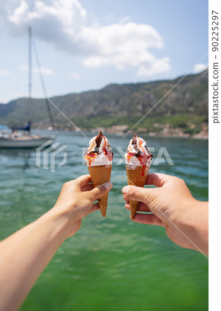 Very beautiful promenade of the Bay of Kotor, Montenegro. Loving couple holding colorful ice cream on the background of the Bay of Kotor. 90225297