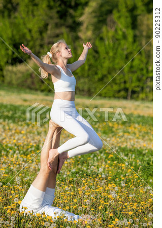 Beautiful young couple doing acro yoga in park. Man lying on grass and balancing woman in his feet. Beautiful young couple doing acro yoga in park. Man lying on grass and balancing woman in his feet. 90225312