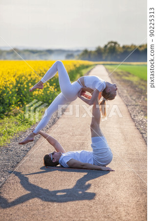 Beautiful young couple doing acro yoga on the bike path. Man lying on road and balancing woman in his feet. Beautiful young couple doing acro yoga on the bike path. Man lying on road and balancing woman in his feet. 90225313