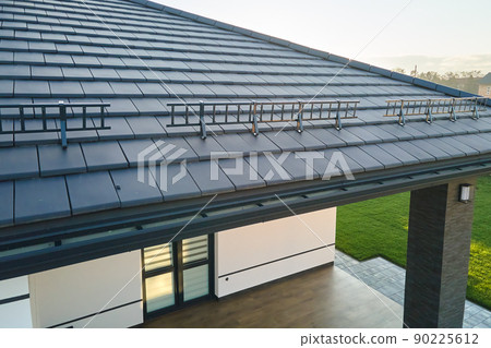 Closeup snow guard for safety in winter on house roof top covered with ceramic shingles. Tiled covering of building 90225612