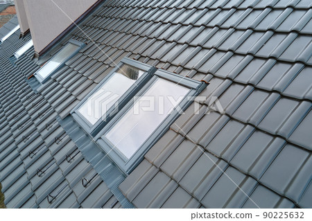 Closeup of attic window on house roof top covered with ceramic shingles. Tiled covering of building Closeup of attic window on house roof top covered with ceramic shingles. Tiled covering of building 90225632