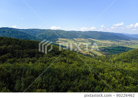 Aerial view of mountain hills covered with dense green lush woods on bright summer day. 90226462