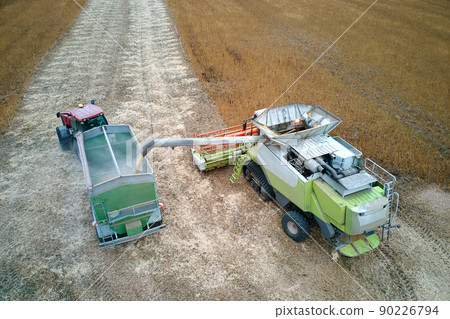 Aerial view of combine harvester unloading grain in cargo trailer working during harvesting season on large ripe wheat field. Agriculture and transportation of raw farm products concept Aerial view of combine harvester unloading grain in cargo trailer working during harvesting season on large ripe wheat field. Agriculture and transportation of raw farm products concept 90226794