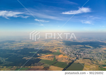 Aerial view from airplane window at high altitude of earth covered with white thin layer of misty haze and distant clouds at sunset Aerial view from airplane window at high altitude of earth covered with white thin layer of misty haze and distant clouds at sunset 90226892