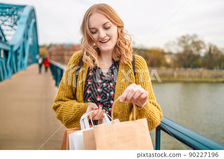Smiling beautiful woman carrying eco paper shopping bags on the bridge in the city Smiling beautiful woman carrying eco paper shopping bags on the bridge in the city 90227196