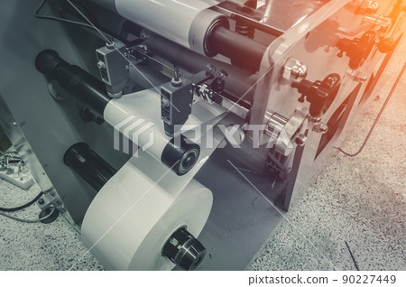 Roller of white printing paper for self-adhesive label on the shaft of the die-cutting machine in the printing house. Selective focus 90227449