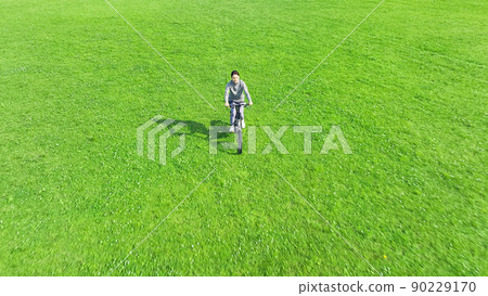 A woman riding a bicycle through the meadow 90229170