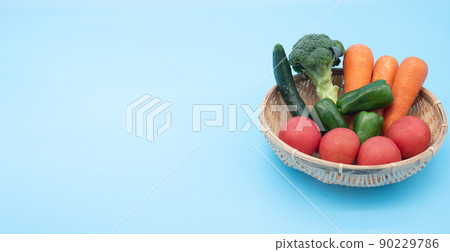 A basket with green and yellow vegetables on a blue background and a copy space on the left 90229786