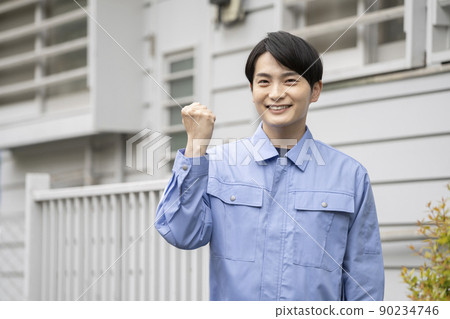 A young man in work clothes standing in front of a house, looking at the camera, portrait A young man in work clothes standing in front of a house, looking at the camera, portrait 90234746