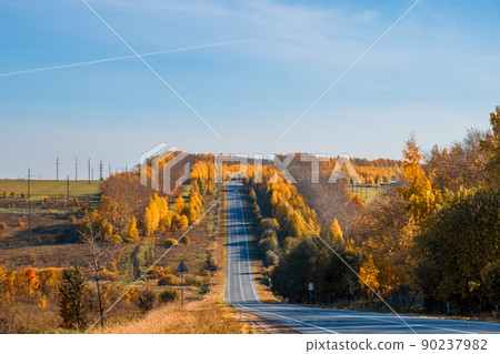 Road through beautiful colored autumn forest and fields. 90237982