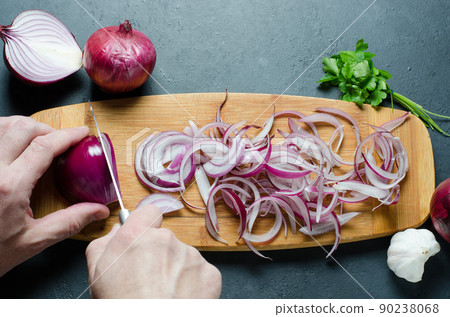 A man cuts red onions on a wooden chopping Board with a kitchen knife. Preparing food. Hands close up. 90238068