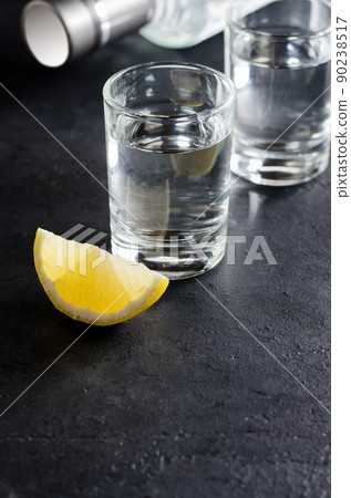 Glasses of vodka on a dark gray background, a piece of lemon, a bottle of vodka. Copy space. Vertical photo 90238517