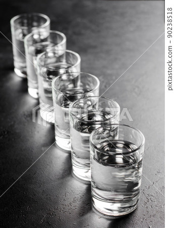 Glasses of vodka are in a row on dark background. Selective focus. Space for text. Vertical photo 90238518