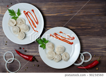 Traditional Russian dumplings, ravioli, dumplings on a white plate with red sauce and parsley. Dark wooden background. Onion rings, chili. Top view. Copy space Traditional Russian dumplings, ravioli, dumplings on a white plate with red sauce and parsley. Dark wooden background. Onion rings, chili. Top view. Copy space 90238560