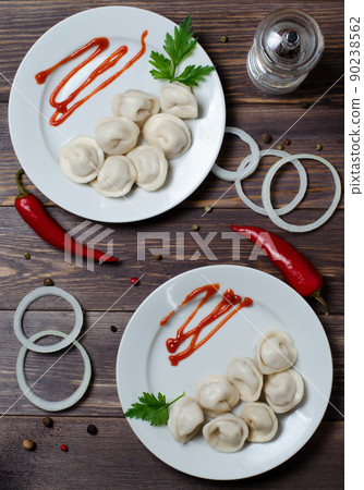 Traditional Russian dumplings, ravioli, dumplings on a white plate with red sauce and parsley. Dark wooden background. Onion rings, chili. Traditional Russian dumplings, ravioli, dumplings on a white plate with red sauce and parsley. Dark wooden background. Onion rings, chili. 90238562