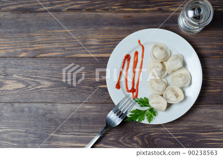 Traditional Russian dumplings, ravioli, dumplings on a white plate with red sauce and parsley. Dark wooden background. Top view. Copy space Traditional Russian dumplings, ravioli, dumplings on a white plate with red sauce and parsley. Dark wooden background. Top view. Copy space 90238563