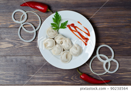Traditional Russian dumplings, ravioli, dumplings on a white plate with red sauce and parsley. Dark wooden background. Onion rings, chili. Traditional Russian dumplings, ravioli, dumplings on a white plate with red sauce and parsley. Dark wooden background. Onion rings, chili. 90238564