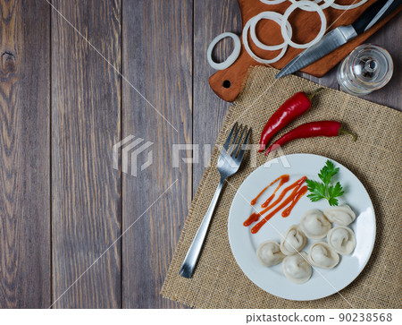 Traditional Russian dumplings, ravioli, pelmeni on a white plate with red sauce and parsley. Dark wooden background. Traditional Russian dumplings, ravioli, pelmeni on a white plate with red sauce and parsley. Dark wooden background. 90238568