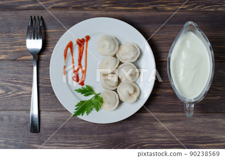 Traditional Russian dumplings, ravioli, pelmeni on a white plate with red sauce and parsley. Dark wooden background. Traditional Russian dumplings, ravioli, pelmeni on a white plate with red sauce and parsley. Dark wooden background. 90238569