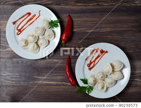 Traditional Russian pelmeni, ravioli, dumplings on a white plate with red sauce and parsley. Dark wooden background. Traditional Russian pelmeni, ravioli, dumplings on a white plate with red sauce and parsley. Dark wooden background. 90238573