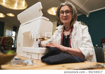 Mature woman sewer in workshop studio, works on sewing machine, designing new collection clothes. Fashion designer business start-up, entrepreneur concept 90238917