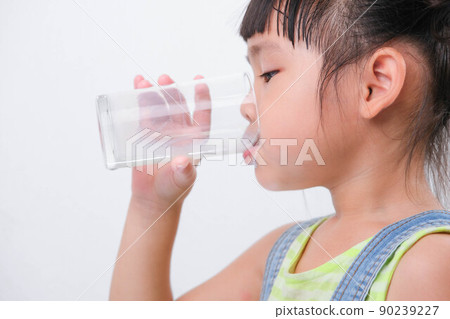 Cute little girl drinking milk from a glass isolated on white background. Little girls enjoy drinking milk before going to school. Cute little girl drinking milk from a glass isolated on white background. Little girls enjoy drinking milk before going to school. 90239227