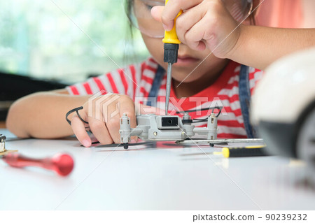 Concentrated little girl repairing her toy drone with a tool in hand and carefully assembles toy drone with screwdriver. STEM Hobbies for advanced smart kids. 90239232