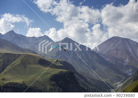 A man on a paraglider takes a selfie. Mountain gorge with green slopes A man on a paraglider takes a selfie. Mountain gorge with green slopes 90239880