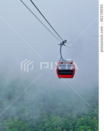 Bright red cable car with double safety sling to the cloudy misty forest in highland mountain in rainy day Bright red cable car with double safety sling to the cloudy misty forest in highland mountain in rainy day 90239893