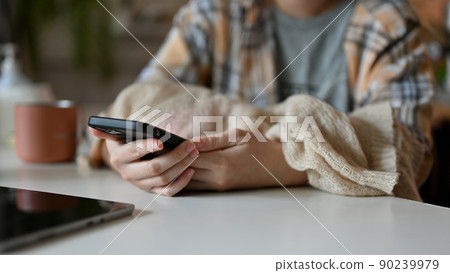Female freelancer sits at her office desk and using smartphone. cropped Female freelancer sits at her office desk and using smartphone. cropped 90239979
