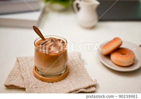 A modern office workspace with an iced latte and a plate with tasty sweet donuts. A modern office workspace with an iced latte and a plate with tasty sweet donuts. 90239981