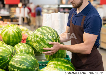 Unrecognizable supermarket worker wearing uniform setting out fresh watermelons, copy space Unrecognizable supermarket worker wearing uniform setting out fresh watermelons, copy space 90240194