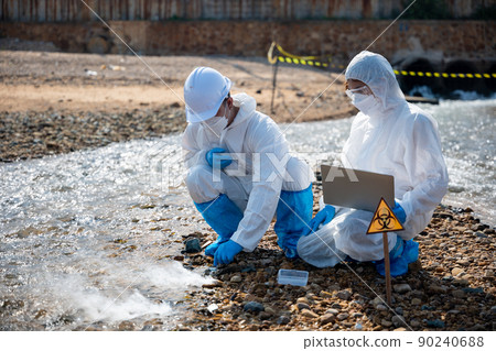 Biologist wear protective suit and mask collects sample of waste water from industry Biologist wear protective suit and mask collects sample of waste water from industry 90240688
