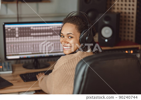 Cheerful African American young female musician, composer, sound engineer working in the music recording studio Cheerful African American young female musician, composer, sound engineer working in the music recording studio 90240744