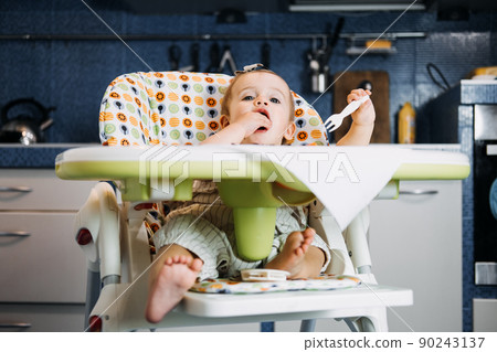 Babys first solid food. Solid food for little child 6 months old. Cute smiling baby girl in high chair eats and tastes with fingers various solid food. Healthy child nutrition. Babys first solid food. Solid food for little child 6 months old. Cute smiling baby girl in high chair eats and tastes with fingers various solid food. Healthy child nutrition. 90243137
