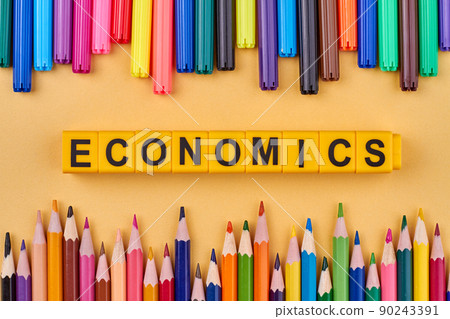 The word ECONOMICS written on plastic cubes in frame from colored school supplies. 90243391