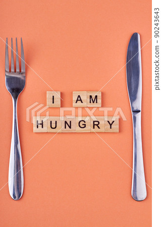 I am hungry inscription on wooden blocks. Fork and knife on table. 90243643