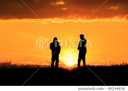 Two silhouettes of men talking at sunset or sunrise with dramatic sky and clouds.Dialogue and meeting two people on the horizon and skyline.Outlines of people in the sunlight.Golden hour with friends 90244636