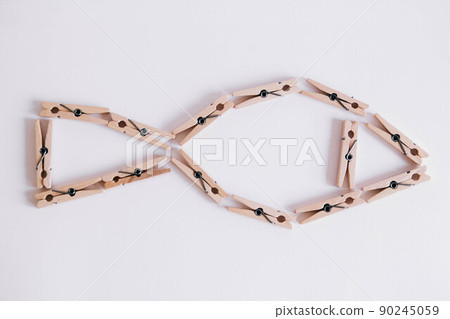 Wooden clothespins on a white background which are composed in the form of a fish icon. View from above. 90245059