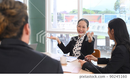 Mature woman team leader talking, giving instructions to diverse staff at corporate office workshop 90245160