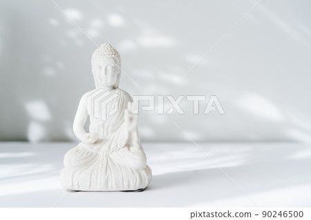 Decorative white Buddha statuette on the white background with sun light shadows. Meditation and relaxation ritual. Buddha birthday. Minimalism. Copy space. Selective focus. Decorative white Buddha statuette on the white background with sun light shadows. Meditation and relaxation ritual. Buddha birthday. Minimalism. Copy space. Selective focus. 90246500