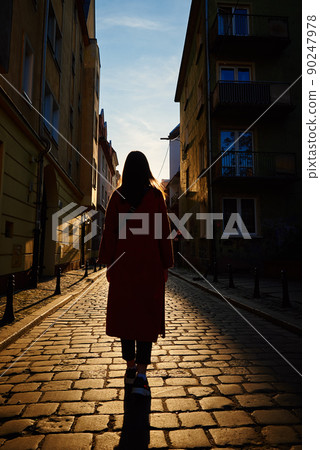 Rear view of tourist woman walking at european city street at sunset, Summer vacation 90247978