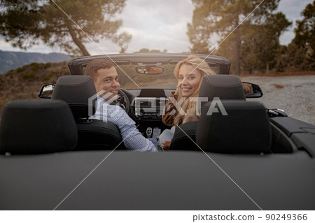 Happy couple of man and woman sitting in a convertible car and smiling while looking back 90249366
