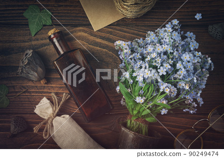 Tincture or potion bottle, sachet of dried herbs, glasses, bouquet of wild forget me not flowers. Top view, flat lay. 90249474