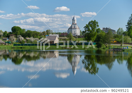 View of the old ancient Church of the Assumption of the Virgin Mary and lake in Derevnoe village, Minsk region, Belarus. 90249521