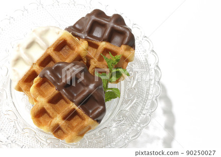 A bird's-eye view of a chocolate-coated waffle on a transparent glass cake stand on a white background A bird's-eye view of a chocolate-coated waffle on a transparent glass cake stand on a white background 90250027