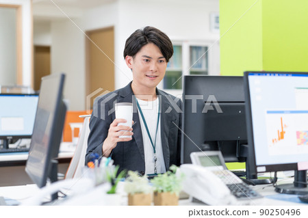 Young businessman drinking a tumbler in the SDGs office Young businessman drinking a tumbler in the SDGs office 90250496