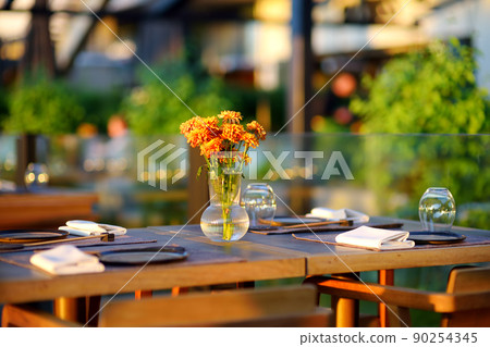 Outdoor cafe on sunny summer day. Stylish table decoration with natural flowers bouquet. Outdoor cafe on sunny summer day. Stylish table decoration with natural flowers bouquet. 90254345
