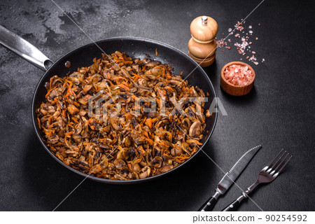 Fried champignons with carrots, onions and spices in a pan against a dark concrete background 90254592